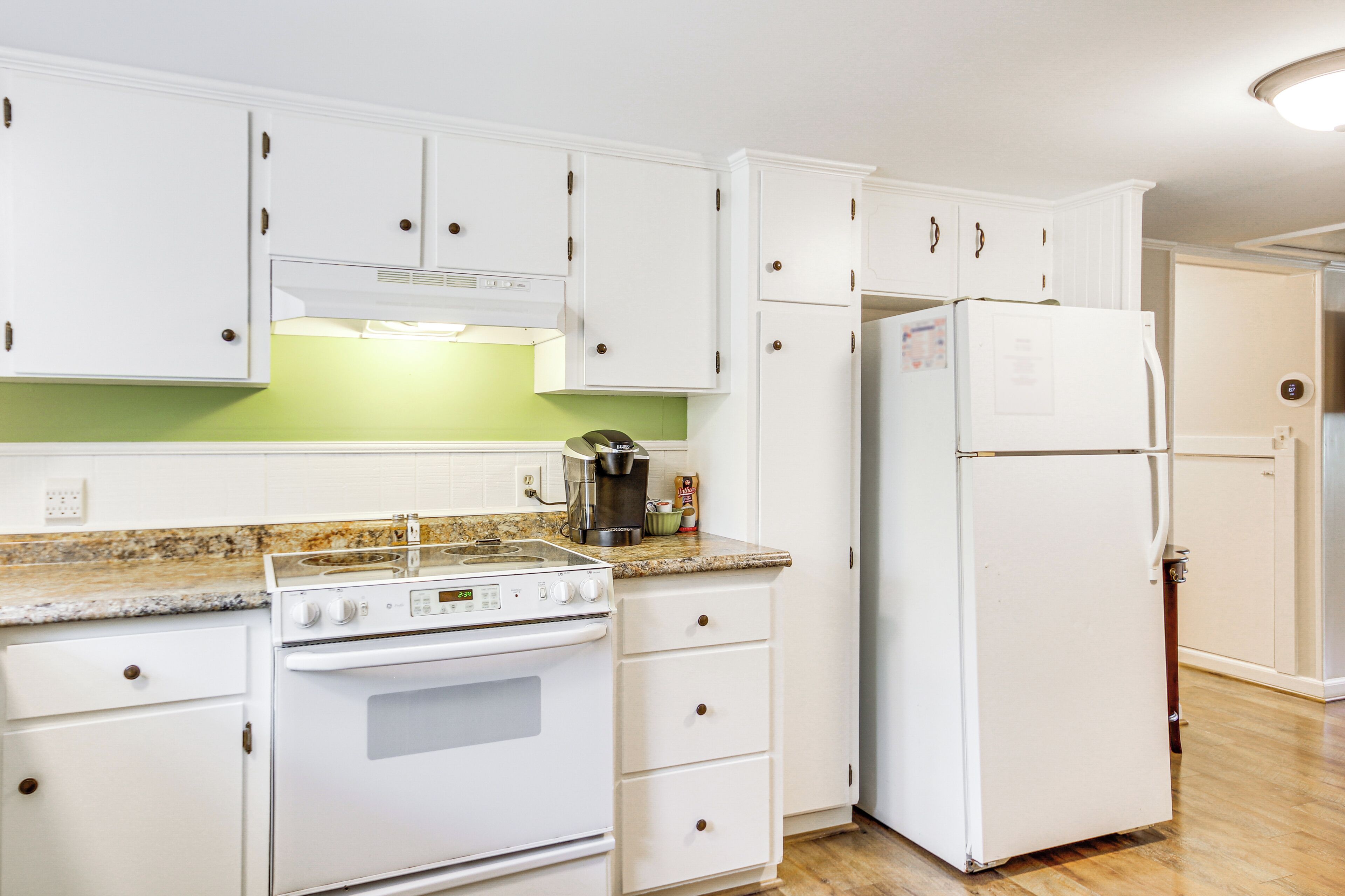 A kitchen with white cabinets, a stove, a refrigerator, and a coffee maker.