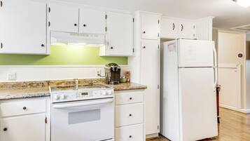 A kitchen with white cabinets, a stove, a refrigerator, and a coffee maker.