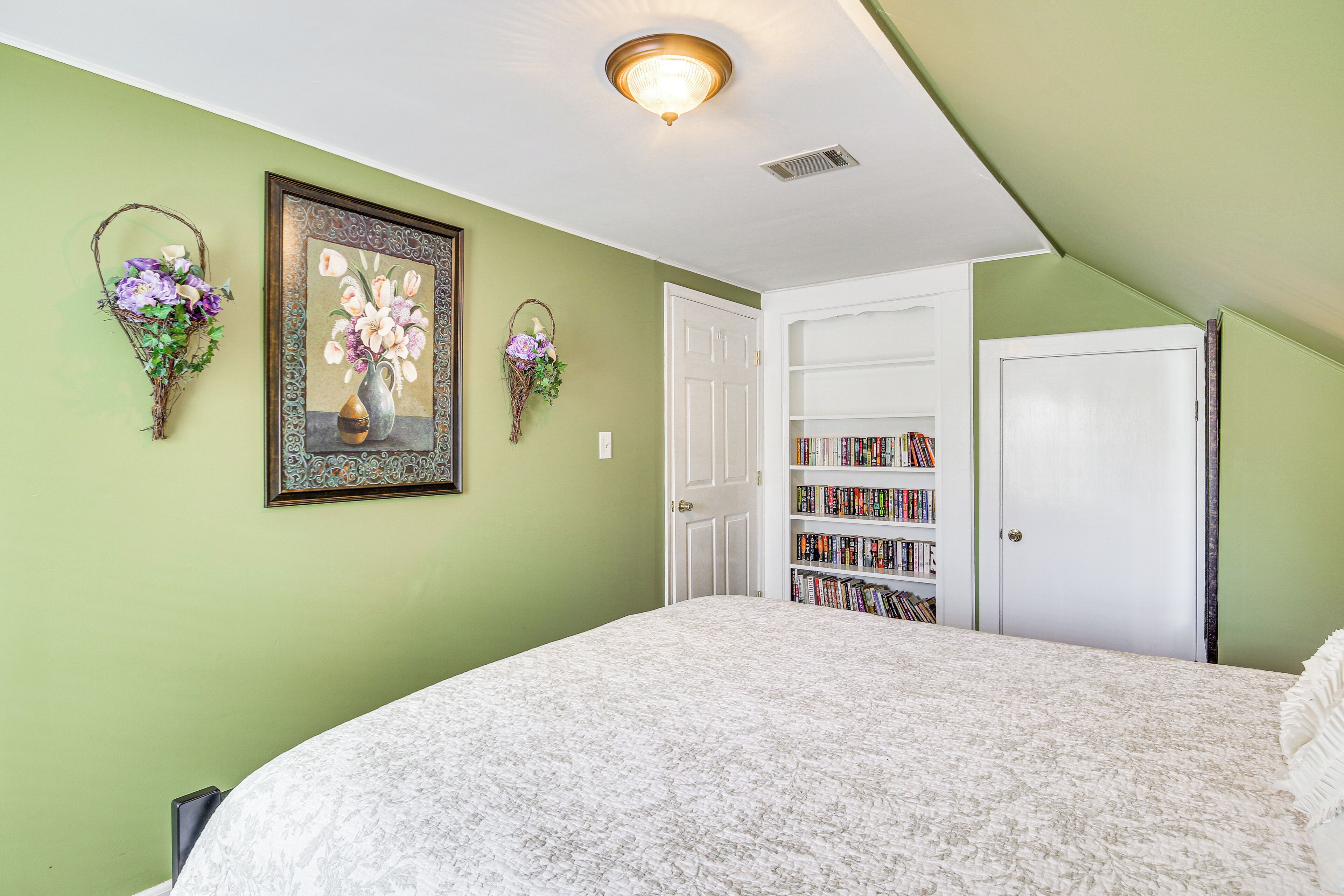 A bedroom with a bed, a bookshelf, and two wall-mounted baskets with flowers.