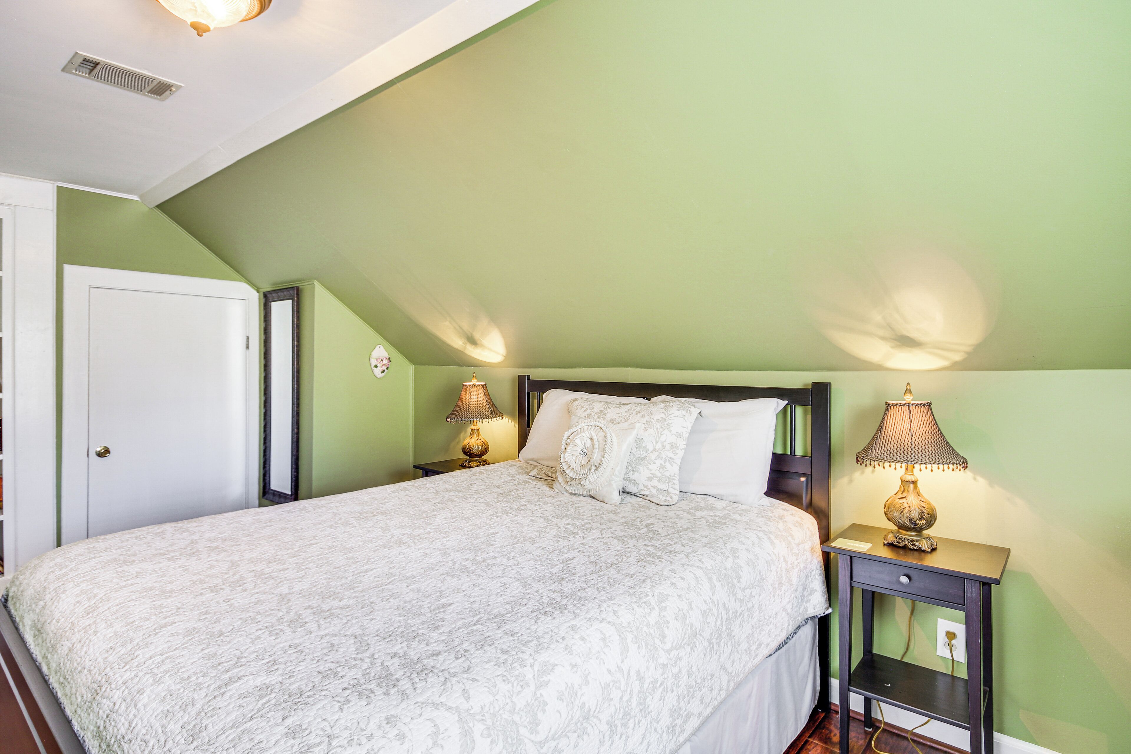 A bedroom with a bed, two bedside lamps, a nightstand, and a door.
