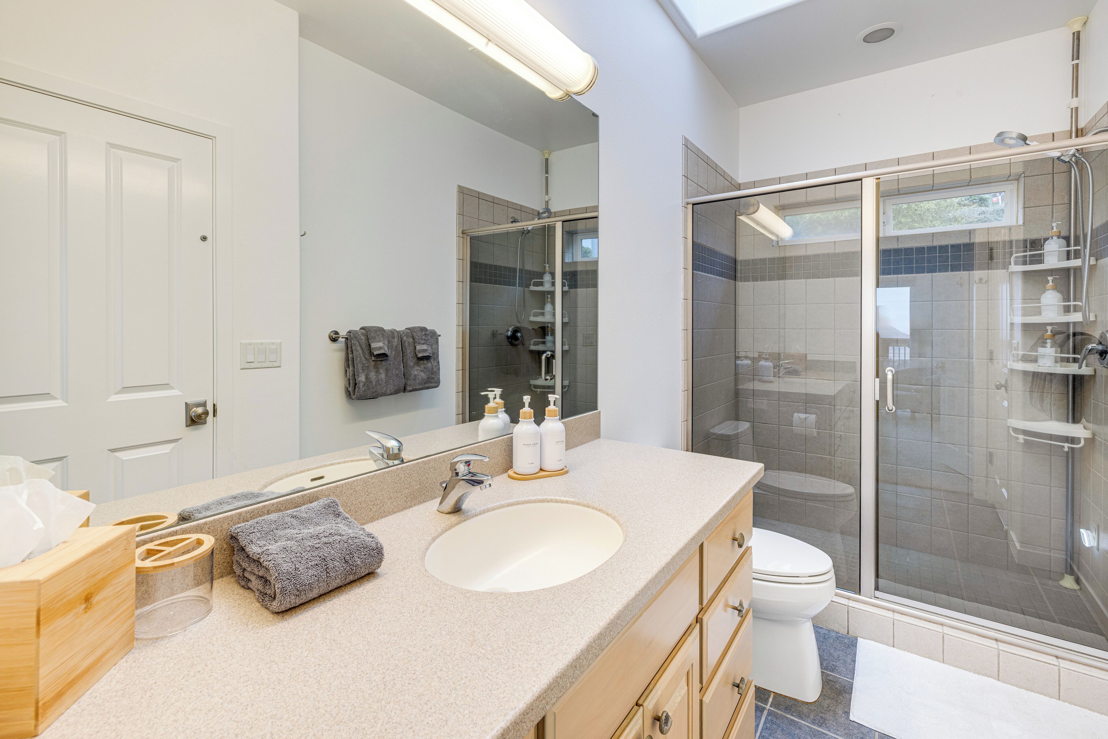 A modern bathroom with a large mirror, a sink, a toilet, and a glass-enclosed shower.