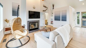A modern living room with a fireplace, a sofa, a rocking chair, and a flat-screen TV. - Lovely Rockaway Beach Home w/ Pacific Ocean Views! (Rockaway Beach)