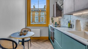 A compact kitchen with a window, a dining table with chairs, and modern appliances. - Hammersmith Residences by MySquare (London)