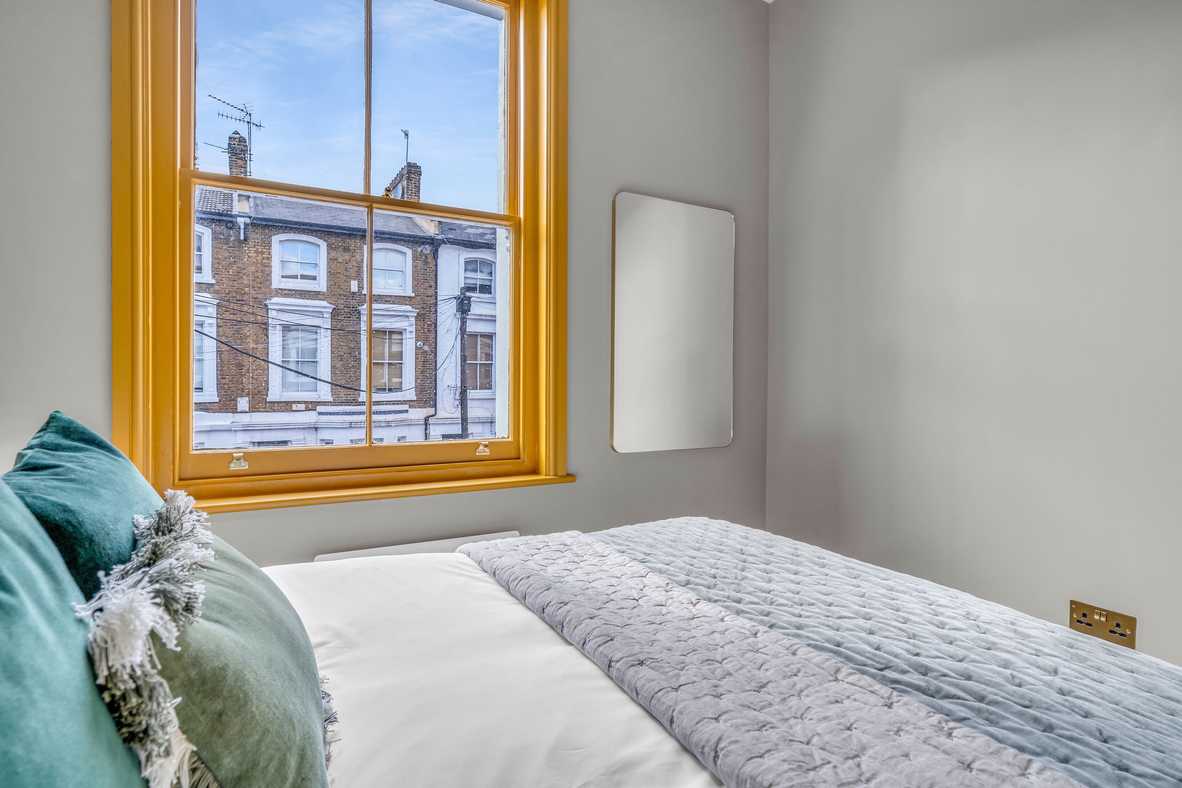 Une chambre à coucher avec un lit, une fenêtre donnant sur des immeubles et un miroir fixé au mur.