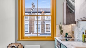 A kitchen with a window, a table with teapots, and a plant on the counter. - Hammersmith Residences by MySquare (London)