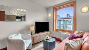 A modern living room with a large flat-screen TV, a comfortable sofa, a white armchair, and a round side table with candles. - Hammersmith Residences by MySquare (London)