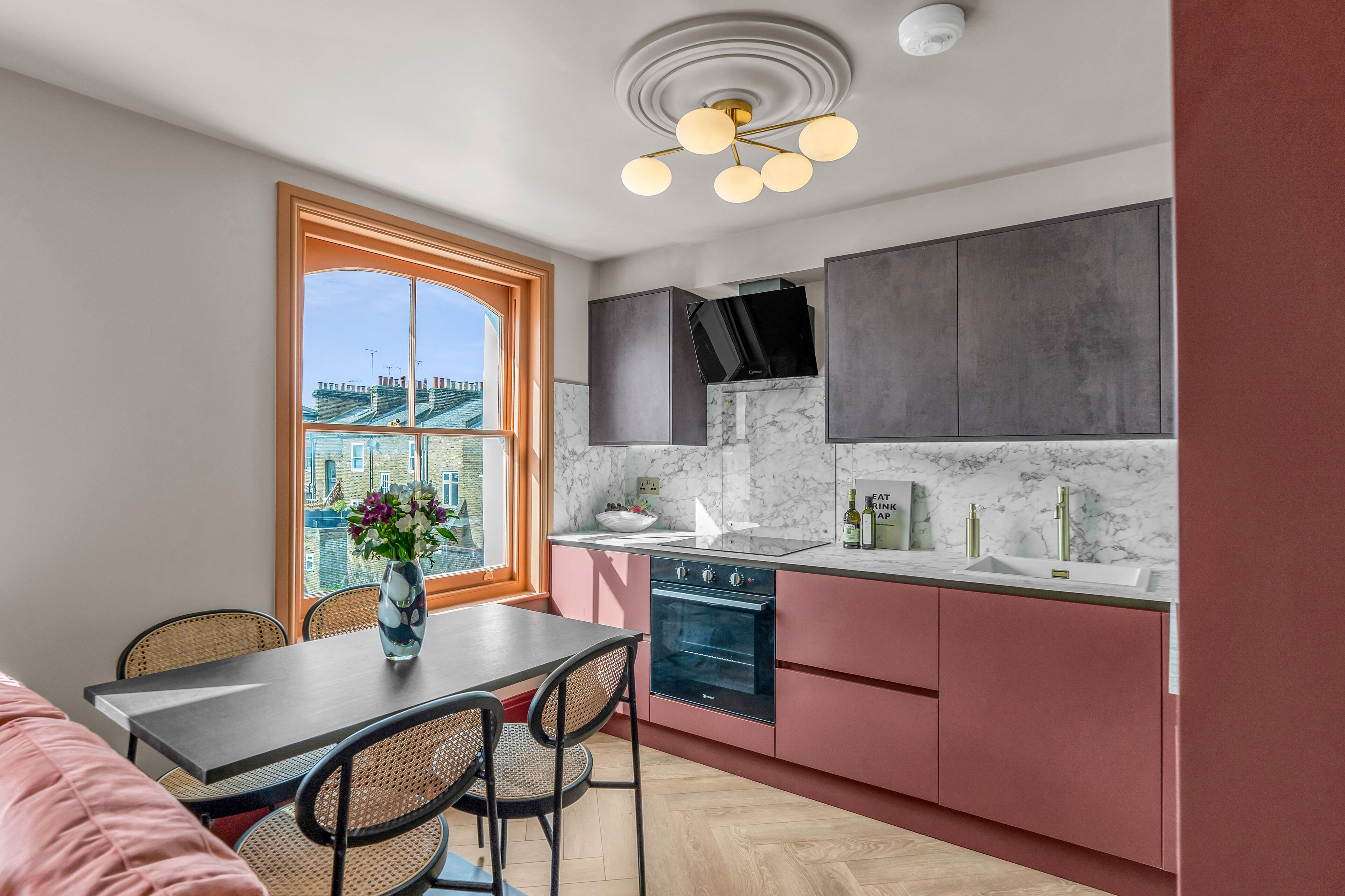 A modern kitchen with a large window, a dining area with a table and chairs, and a view of buildings outside.