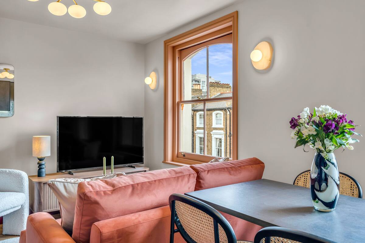 A modern living room with a large TV, comfortable seating, a dining table, and a window with a view of buildings.