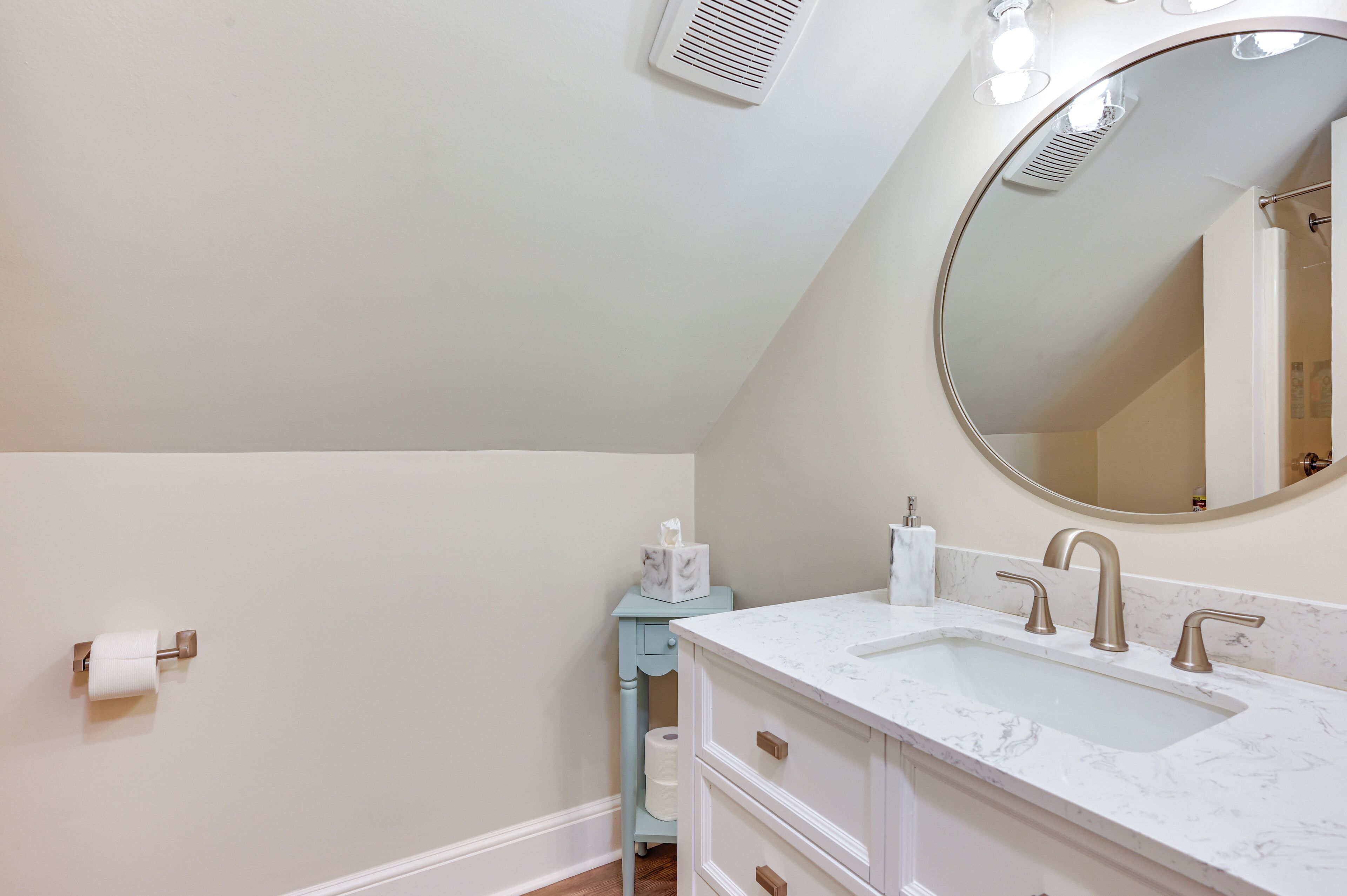A bathroom with a white sink, a mirror, and a toilet paper holder.