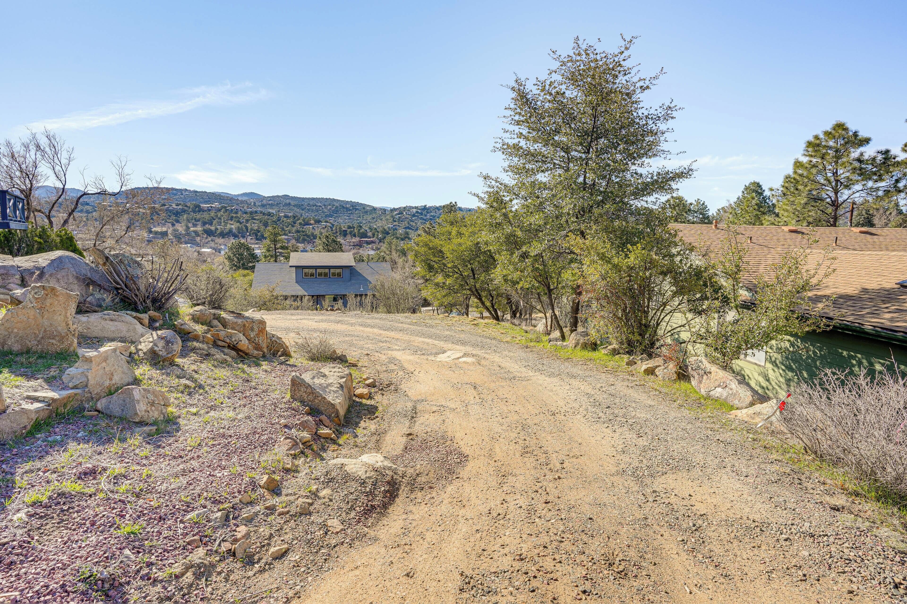 A rural road leading to a house with a sloped roof, surrounded by rocks and sparse vegetation.