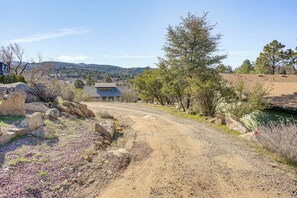 Un chemin de campagne menant à une maison au toit en pente, entourée de rochers et d’une végétation clairsemée.