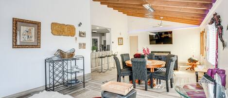 A modern living room with a dining area, wooden ceiling beams, a TV, and various decorative items.