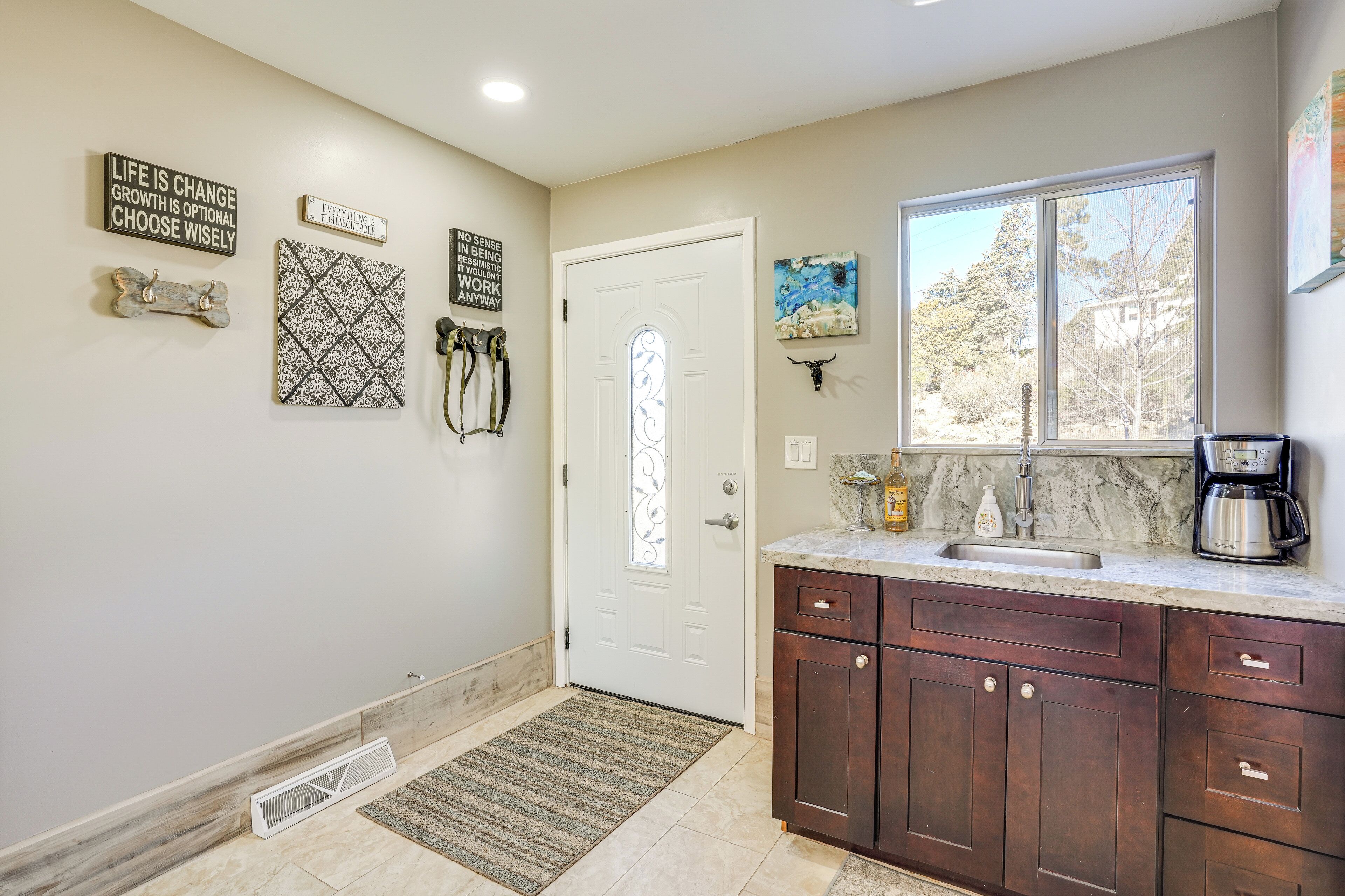 A kitchen with a white door, dark wooden cabinets, a marble countertop, and a window with a view of trees.