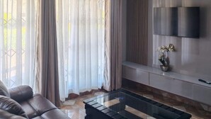 Ein modernes Wohnzimmer mit einer Ledersofa, einem Glastisch, einem flachbildfernseher an der Wand und einer Topfpflanze auf einer Konsole.