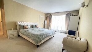 A bedroom with a large bed, a nightstand, a chair, and a mirror. - Tussauds Appartment (London)