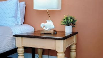 A bedroom with a bed, a nightstand with a lamp, a small plant, and a colorful rug.