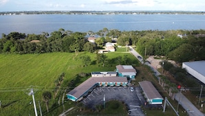 An aerial view of a coastal property with a large parking lot, a building with a blue and white facade, and a view of the sea. - Bonsai - A Modern Motor Court (Rockledge)