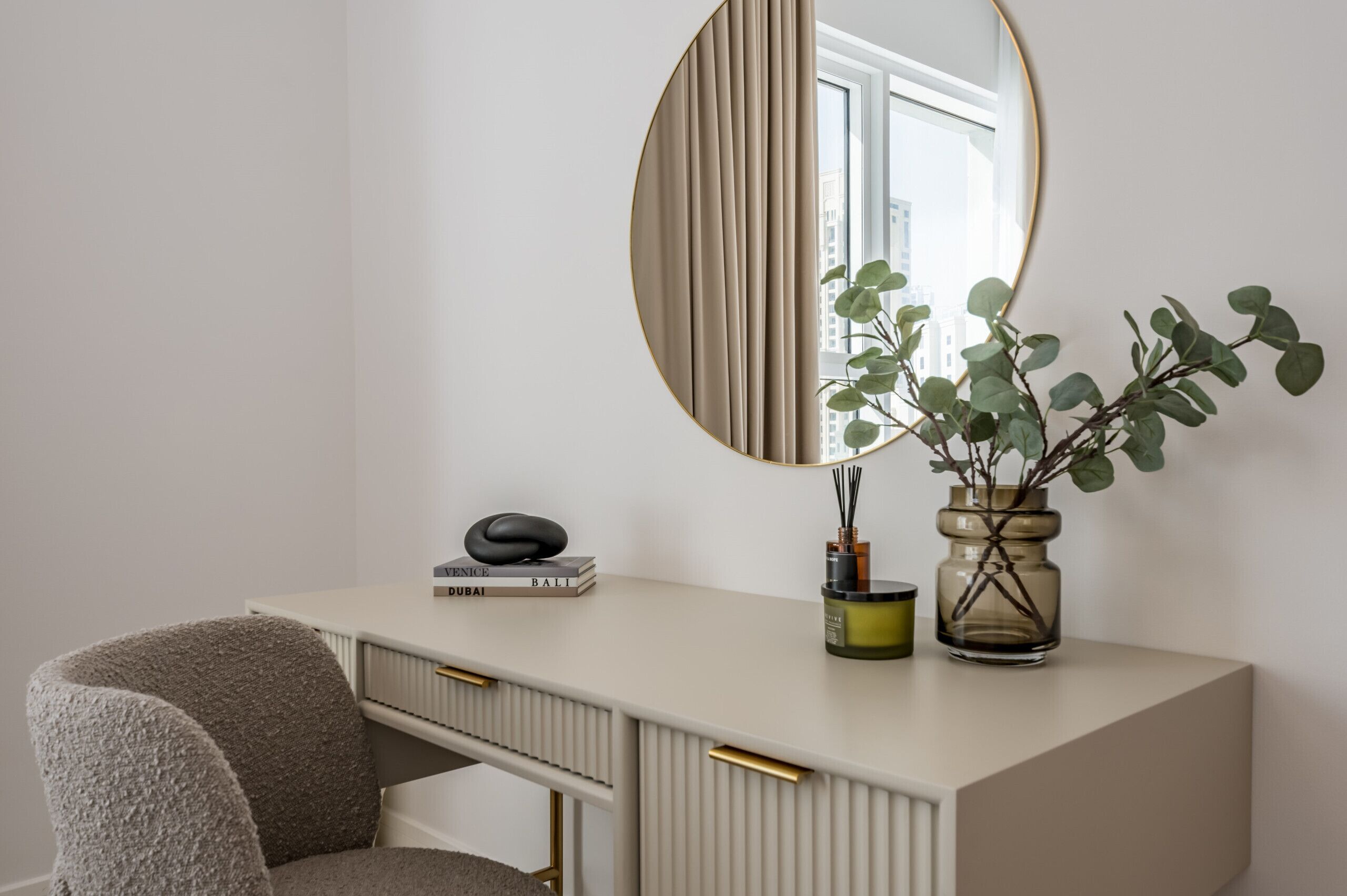 Un bureau moderne et épuré, agrémenté d’un miroir rond, d’une plante en pot et d’une pile de livres.