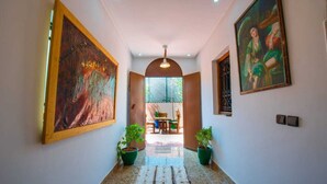 A hallway with large paintings on the walls, potted plants, and a view into a dining area.