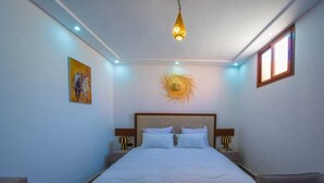 A bedroom with a large bed, a ceiling light, a painting on the wall, and a window.