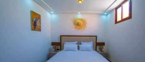 Un dormitorio con una cama grande, una lámpara en el techo, un cuadro en la pared y una ventana.