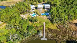 Vue aérienne d’une propriété dotée d’une piscine, d’un court de tennis et d’une jetée s’avançant dans une étendue d’eau.