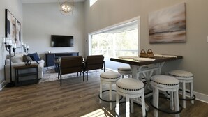 A spacious living area with a dining table, bar stools, and a flat-screen TV mounted on the wall. - The Clermont at Clermont Bay (Hancock County)