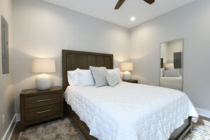 A neatly arranged bedroom with a large bed, two bedside tables with lamps, a wooden headboard, and a mirror on the wall. - The Clermont at Clermont Bay (Hancock County)