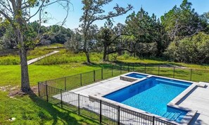 A rectangular swimming pool with a black metal fence surrounding it, set in a grassy area with trees in the background. - The Clermont at Clermont Bay (Hancock County)