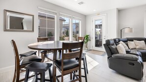 A modern living room with a dining table, chairs, a sofa, and a large window with blinds. - Haven in the Sand: 4 beds 3.5 baths, sleeps 10.  Community Pool. (Washington)
