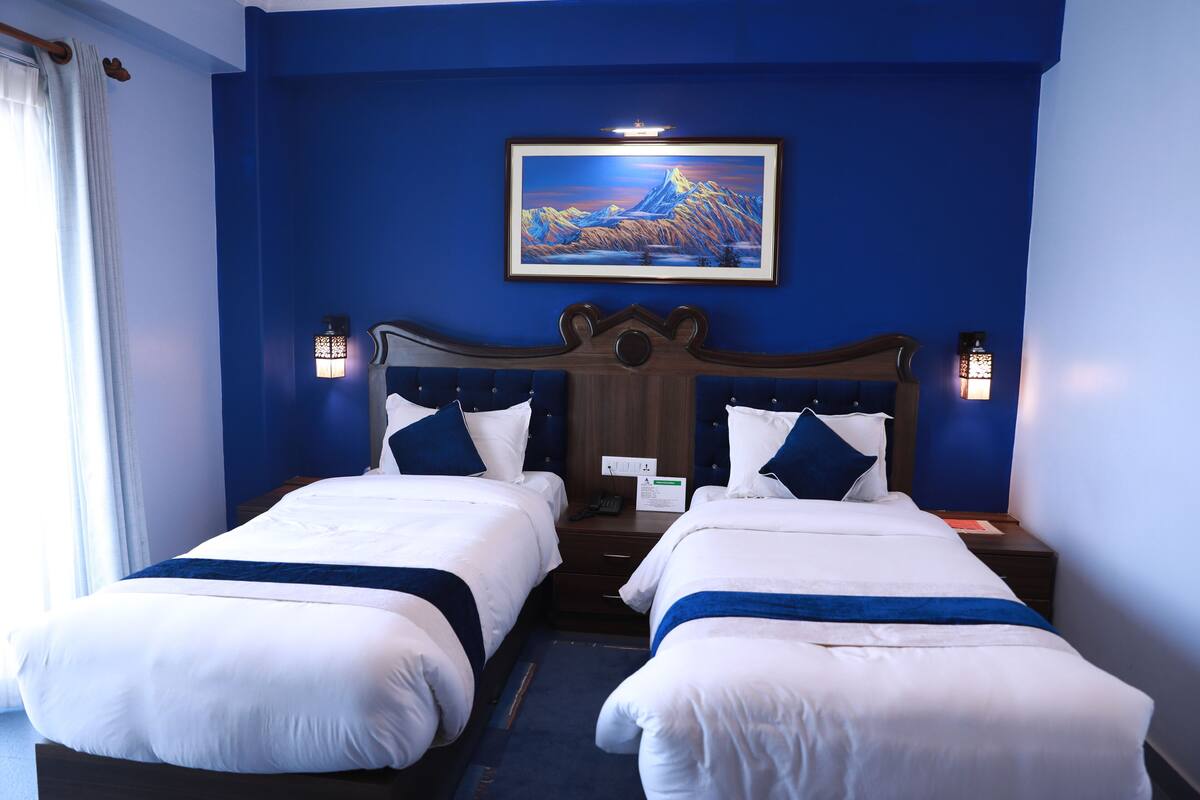 Quarto de hotel com duas camas, uma pintura grande na parede e duas luminárias fixadas na parede.