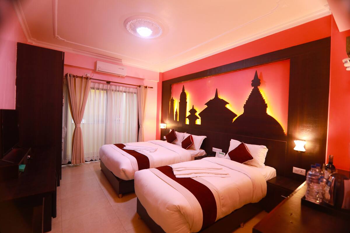 Quarto de hotel com duas camas, televisão, escrivaninha e parede com mural da paisagem urbana.