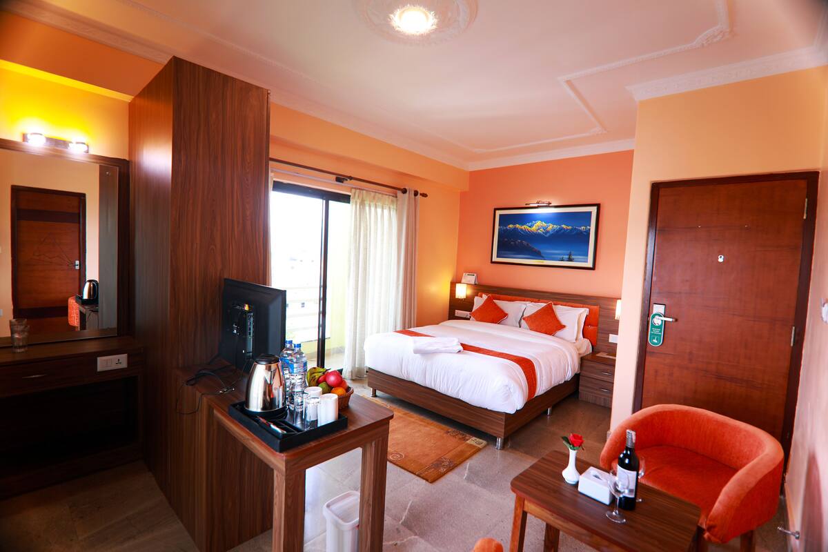 Quarto de hotel com uma cama, uma escrivaninha com televisão, uma cadeira e uma mesa com garrafa e copo.