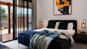 A bedroom with a bed, a nightstand, a lamp, and a sliding glass door leading to an outdoor area. - Wynvale Cottage @ Hepburn (Hepburn)