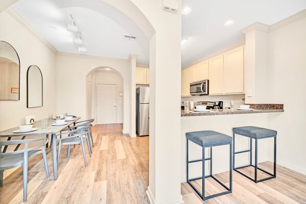 A modern kitchen with a central island, stainless steel appliances, and a bar area with stools. - Upstay: Resort Style Condo w Pool, Sauna (Winter Garden)