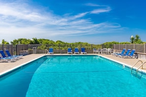 Ein rechteckiger Swimmingpool mit klarem, blauem Wasser, umgeben von blauen und weißen Liegestühlen.