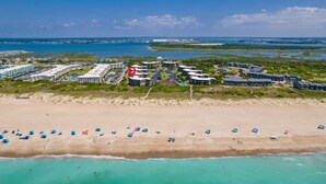 An aerial view of a coastal hotel with multiple buildings, a sandy beach, and a clear blue sea. - Seabound - Oceanfront Condo + Steps to the Sand (Atlantic Beach)
