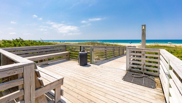 A wooden boardwalk leading to a beach with a clock tower, benches, and a trash can. - Seabound - Oceanfront Condo + Steps to the Sand (Atlantic Beach)