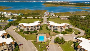 A residential area with two multi-story buildings, a swimming pool, and a marina in the background. - Seabound - Oceanfront Condo + Steps to the Sand (Atlantic Beach)