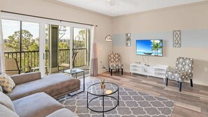 Ein großzügiges Wohnzimmer mit großem Fernseher, bequemen Sitzgelegenheiten und einem Balkon mit Blick.