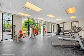 Un gimnasio con equipo de ejercicio, ventanas amplias y vista a zonas verdes.
