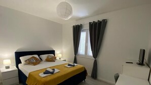 A bedroom with a bed, bedside tables, a desk, a chair, a lamp, a television, and a window with curtains.