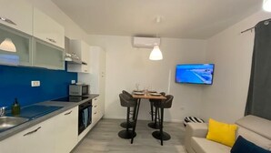 A compact kitchen with a dining area, a flat-screen TV, and a sofa with cushions.