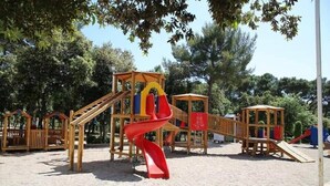 A playground with wooden structures, including a slide and climbing areas, surrounded by trees.