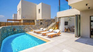 A modern pool area with a clear blue pool, sun loungers, and a stone wall. - Stefi Deluxe Villas - Avgi Private Pool Retreat (Anopoli)