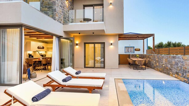 A modern outdoor pool area with lounge chairs, a dining set, and a stone wall. - Stefi Deluxe Villas - Avgi Private Pool Retreat (Anopoli)