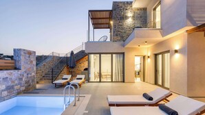 Ein moderner Poolbereich im Freien mit Liegestühlen, einer Steinmauer und einer Treppe, die zu einem Balkon führt.