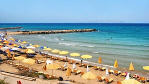 Una spiaggia con file di lettini e ombrelloni, un molo roccioso e acqua cristallina.