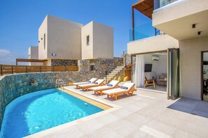 A modern pool area with a clear blue pool, sun loungers, and a stone wall. - Stefi Deluxe Villas - Iris Private Pool Retreat (Anopoli)