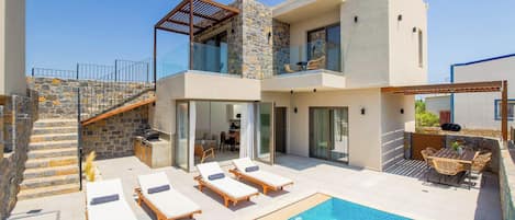 A modern two-story house with a swimming pool, outdoor seating, and a stone staircase.